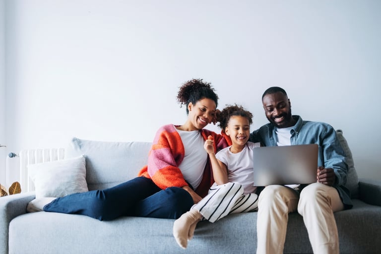 Joyful family sitting together on a cozy sofa looking at a laptop