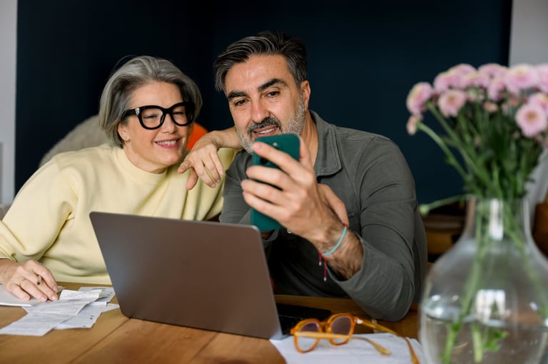 Mature couple sitting at home managing their finances with a laptop and smartphone